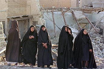 Five Iraqi women in black robes walking through a bomb-damaged street